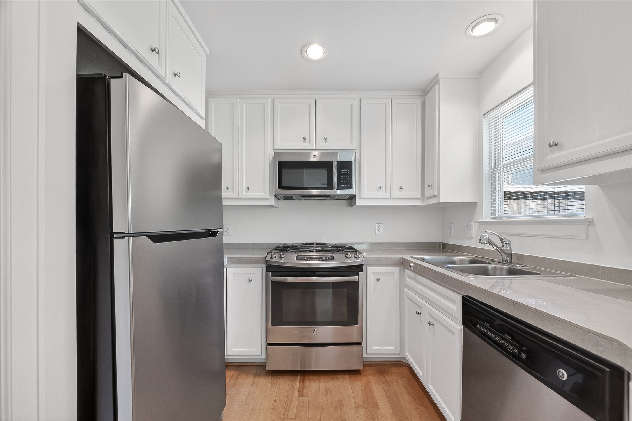5951 S Loop East, Unit 47 Houston, TX 77033 - Photo 12 of 37 This kitchen features modern stainless steel appliances, white cabinetry, and a neutral countertop, providing a clean and functional space with natural light from a side window.