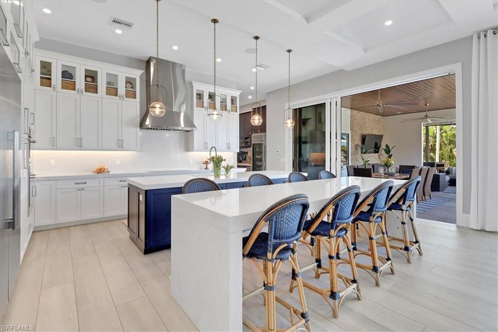 1425 Crayton Road Naples, FL 34102 - Photo 6 of 31 Kitchen with light wood-type flooring, hanging light fixtures, white cabinets, wall chimney exhaust hood, and a center island