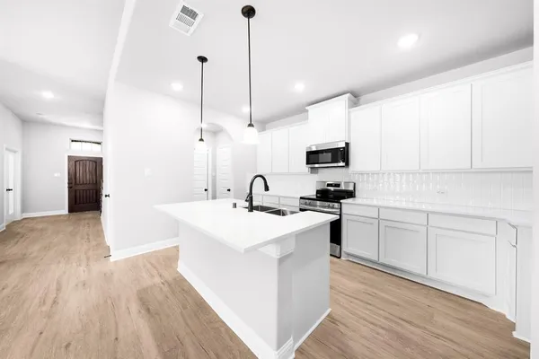 a view of a kitchen with kitchen island a sink stainless steel appliances and white cabinets
