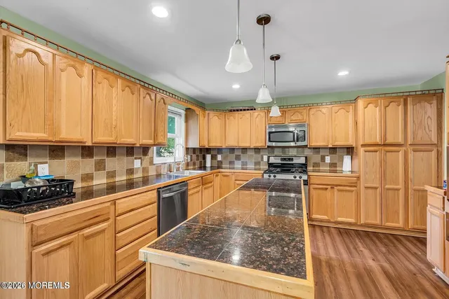 a kitchen with stainless steel appliances granite countertop a refrigerator a sink dishwasher a stove and white cabinets with wooden floor