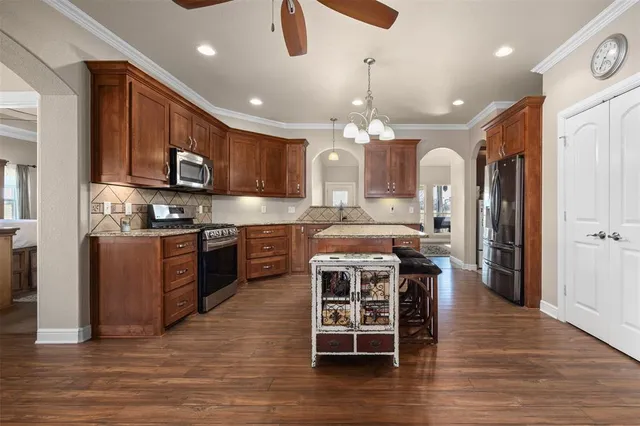 a kitchen with stainless steel appliances kitchen island granite countertop a stove top oven a sink dishwasher a dining table and chairs with wooden floor