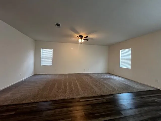 an empty room with wooden floor fan and windows