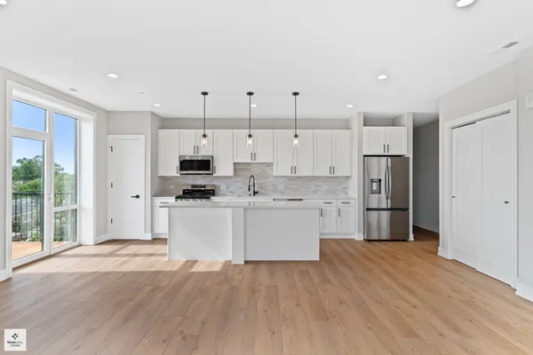 a kitchen with stainless steel appliances kitchen island granite countertop a refrigerator a sink and white cabinets with wooden floor