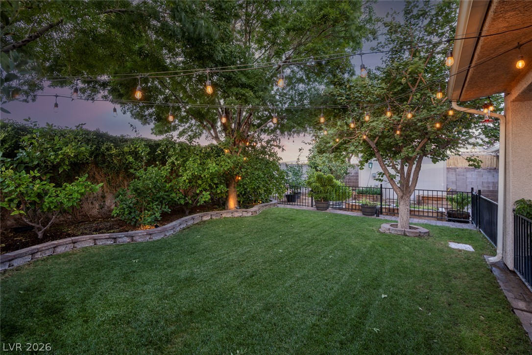 818 Manor Shores Road Henderson, NV 89002 - Photo 35 of 35 Lush green lawn and mature trees define this private yard, illuminated by charming string lights.