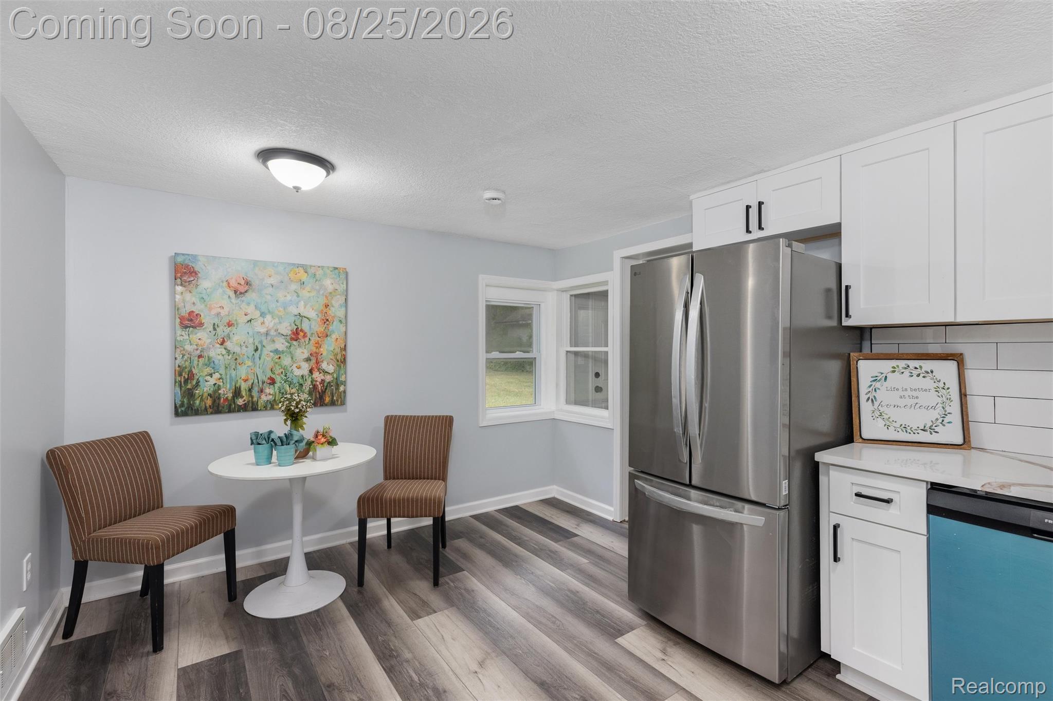 1156 Rinn Street Burton, MI 48509 - Photo 12 of 25 White shaker cabinetry with matte black hardware, stainless steel refrigerator, subway tile backsplash, light countertops, and wood-finish flooring