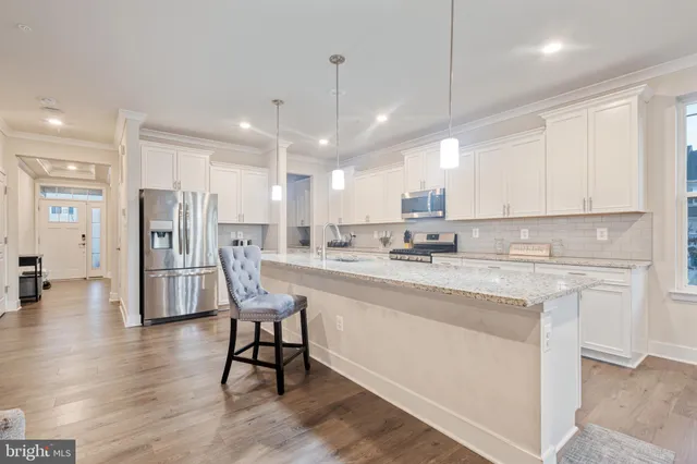 a open kitchen with stainless steel appliances granite countertop a stove a sink a refrigerator and white cabinets with wooden floor