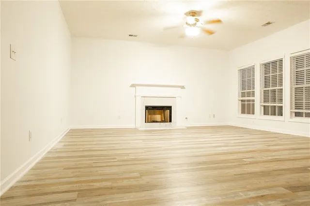 a view of an empty room with wooden floor and a ceiling fan