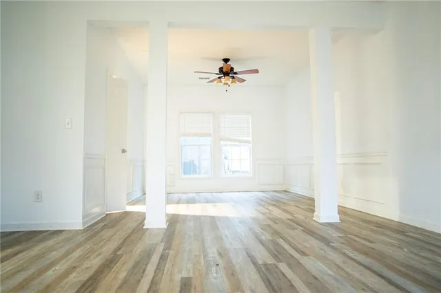 an empty room with wooden floor ceiling fan and windows