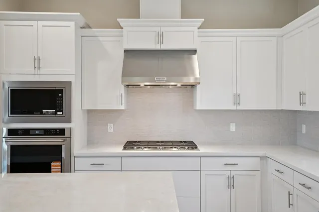 a large white kitchen with granite countertop a sink and white cabinets with wooden floor