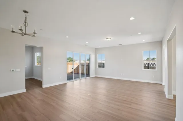 a view of an empty room with wooden floor and kitchen space