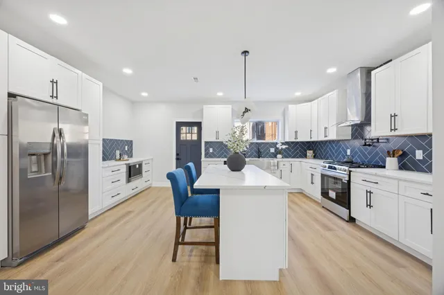 a large kitchen with stainless steel appliances kitchen island granite countertop a refrigerator a stove a sink a dining table and chairs with wooden floor