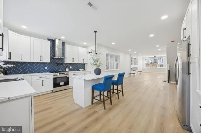 a large white kitchen with lots of counter space a sink refrigerator and chairs