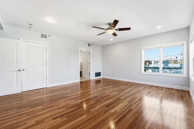 a view of empty room with wooden floor and fan