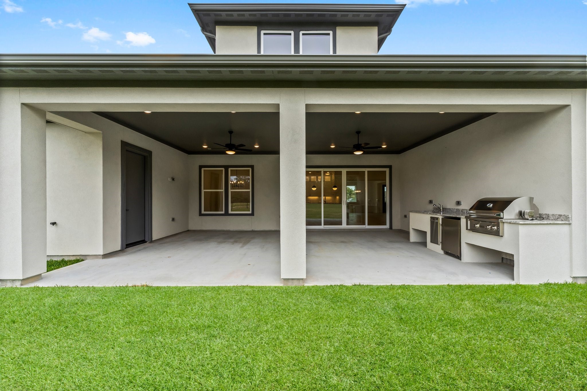 7315 Julie Pond Lane Spring, TX 77389 - Photo 43 of 48 Covered patio with a built-in outdoor kitchen, including a grill and countertop. The area features ceiling fans and is adjacent to a lush green lawn, perfect for entertaining and relaxation.