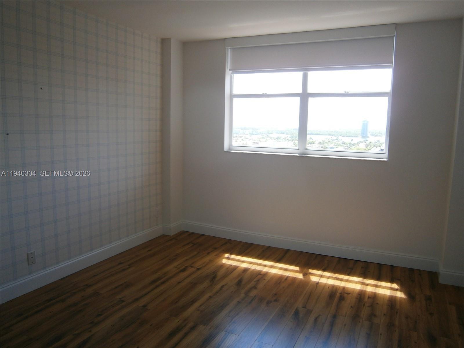 290 174th Street, Unit 1908 Sunny Isles Beach, FL 33160 - Photo 17 of 29 a view of an empty room with wooden floor and a window