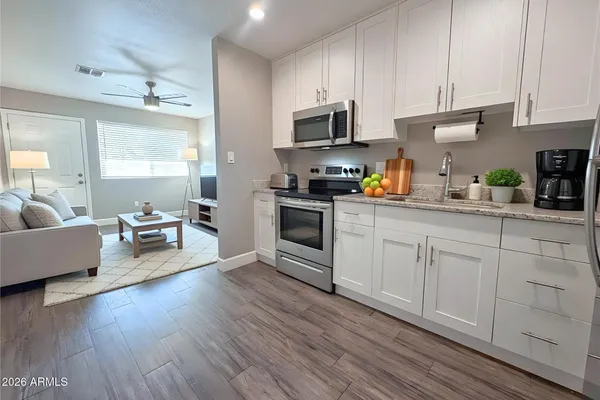 a kitchen with stainless steel appliances granite countertop a refrigerator a stove a sink dishwasher and white cabinets with wooden floor