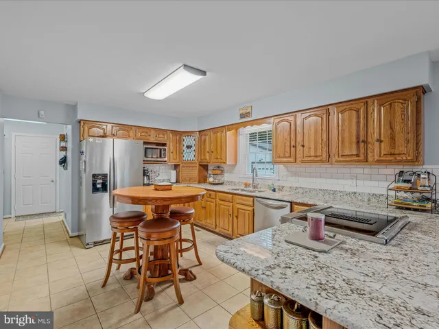 a dining hall with stainless steel appliances kitchen island granite countertop a table chairs sink and cabinets