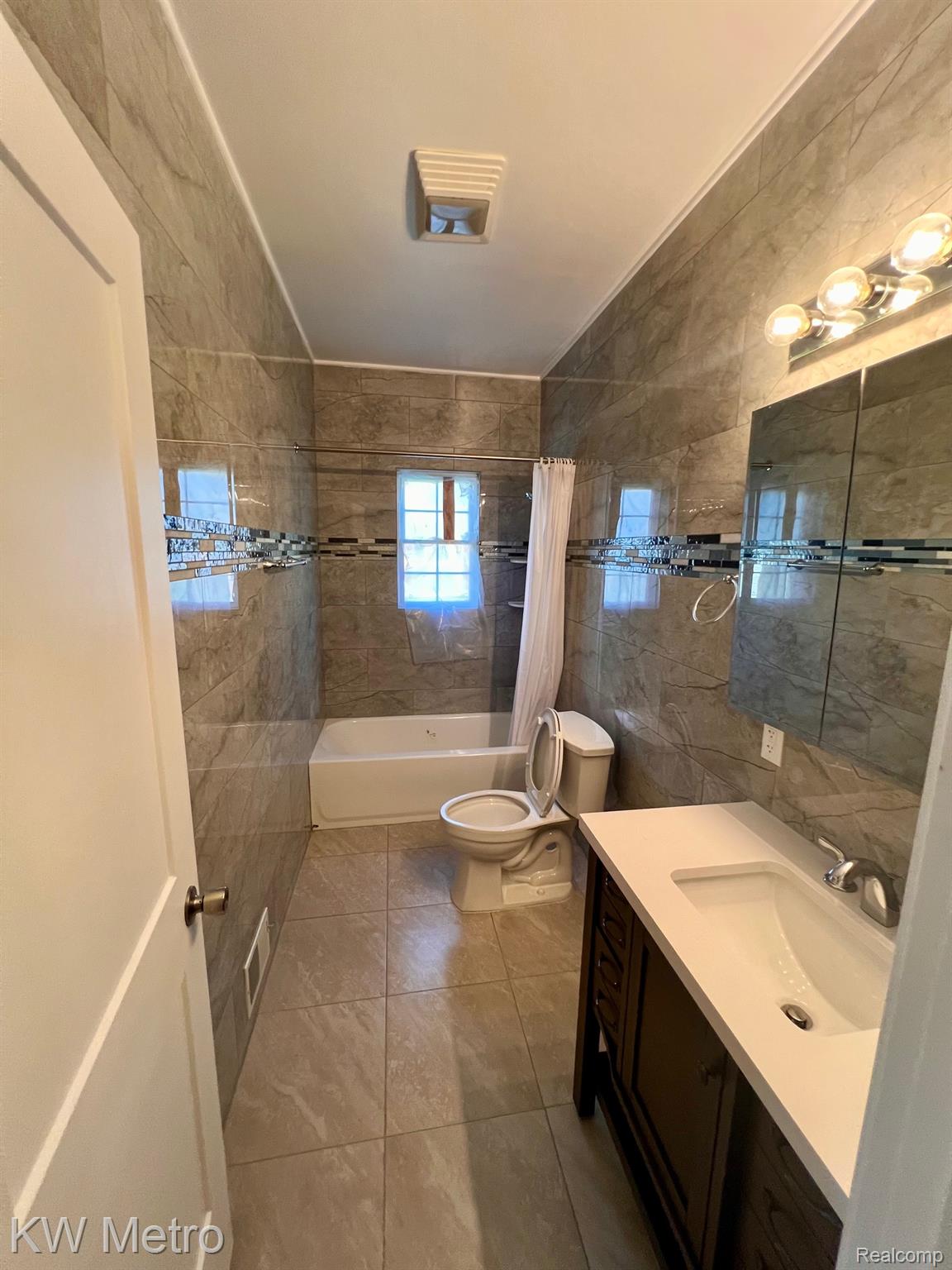 939 Webb Street Detroit, MI 48202 - Photo 5 of 19 Bathroom featuring floor-to-ceiling tile, a single vanity with a white countertop and undermount sink, a mirrored medicine cabinet, and a bathtub with an overhead shower
