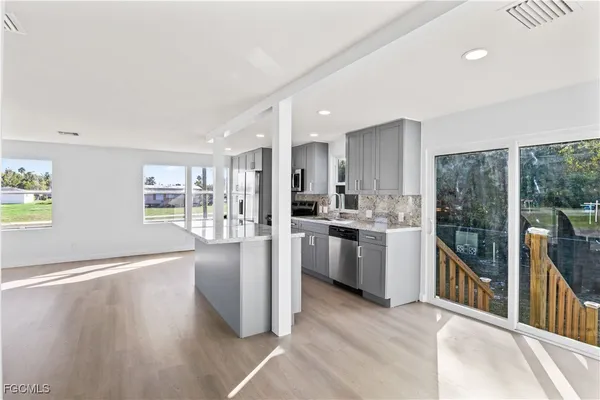 a kitchen with stainless steel appliances kitchen island granite countertop a refrigerator oven a sink dishwasher and white cabinets with wooden floor
