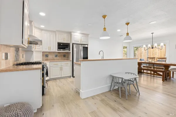 a kitchen with stainless steel appliances granite countertop a stove top oven a sink dishwasher a dining table and chairs with wooden floor