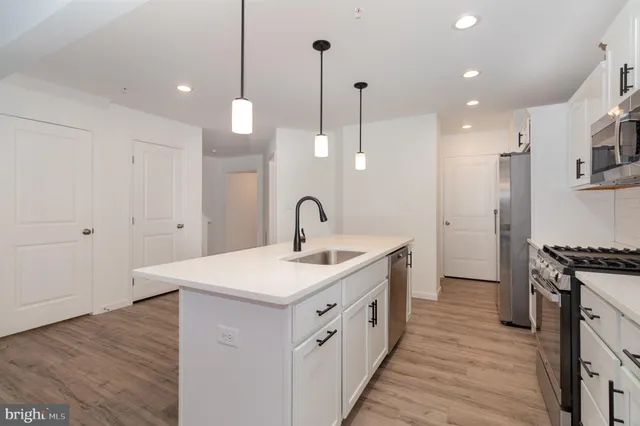 a kitchen with stainless steel appliances a sink a stove a refrigerator a center island and a wooden floor