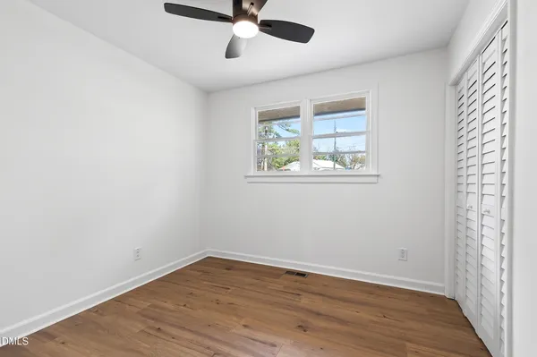an empty room with wooden floor fan and windows