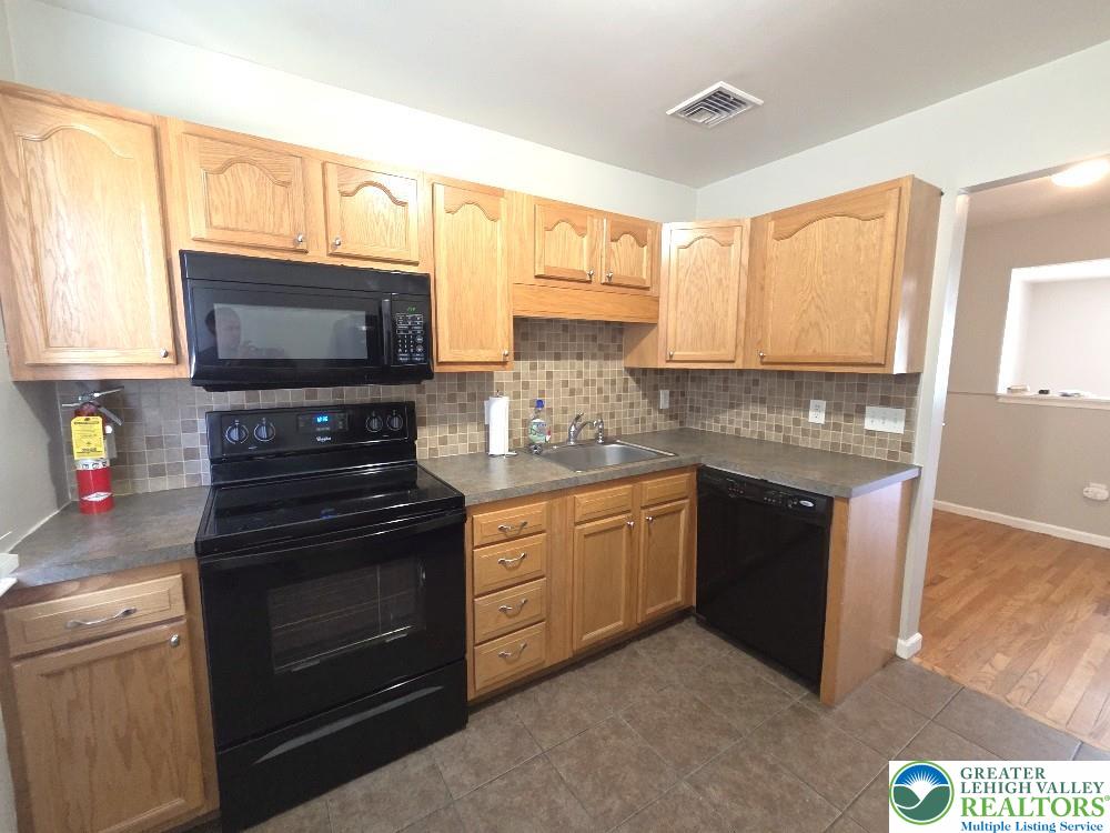 1747 Schoenersville Road Bethlehem, PA 18018 - Photo 7 of 13 A well-appointed kitchen features black appliances, light wood cabinetry, and a tile backsplash, with durable tile flooring.