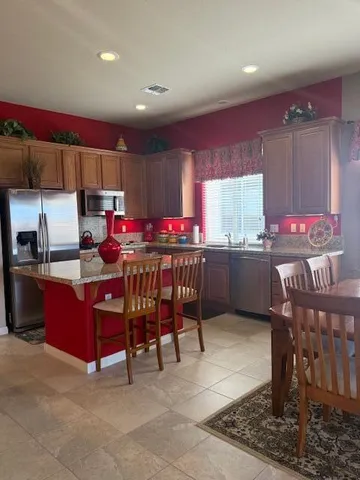a kitchen with stainless steel appliances kitchen island granite countertop a table chairs in it and a window