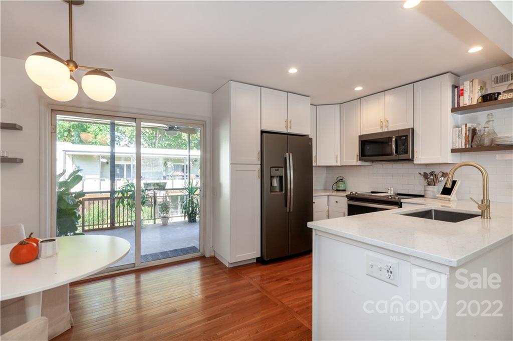 a kitchen that has a microwave a stove a refrigerator a sink and a dining table with wooden floor