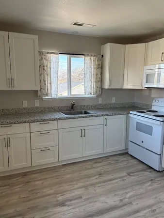 a kitchen with granite countertop white cabinets white appliances with a sink and dishwasher with wooden floor