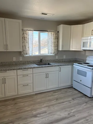 a kitchen with granite countertop white cabinets white appliances with a sink and dishwasher with wooden floor