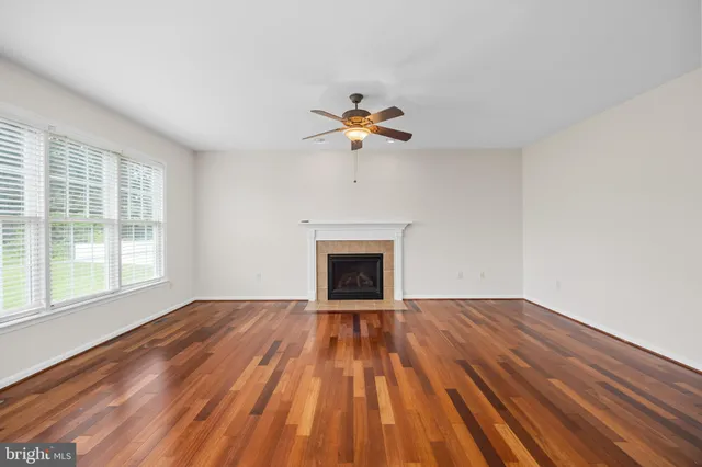 a view of an empty room with wooden floor and a ceiling fan