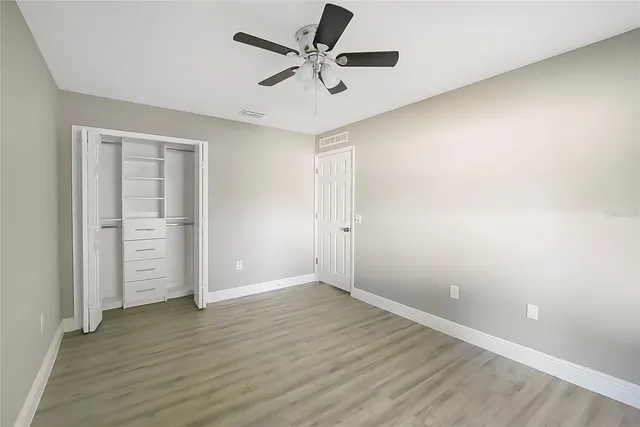 an empty room with wooden floor and ceiling fan