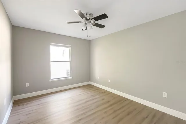 an empty room with wooden floor fan and windows