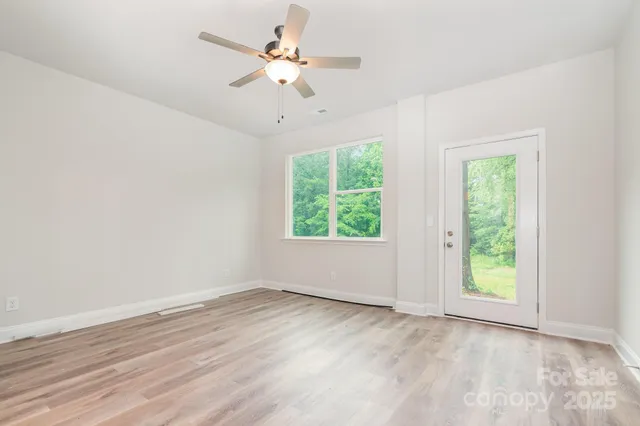 an empty room with wooden floor chandelier fan and windows