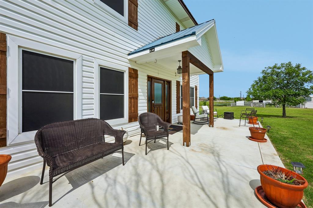 331 Radecke Road Krum, TX 76249 - Photo 4 of 40 Spacious concrete porch featuring a wood-beam covered entry, white siding, dark wood shutters, and a metal roof accent