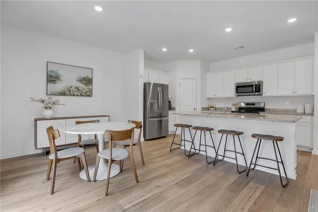 a kitchen with stainless steel appliances granite countertop a stove top oven a refrigerator a sink and white cabinets with wooden floor