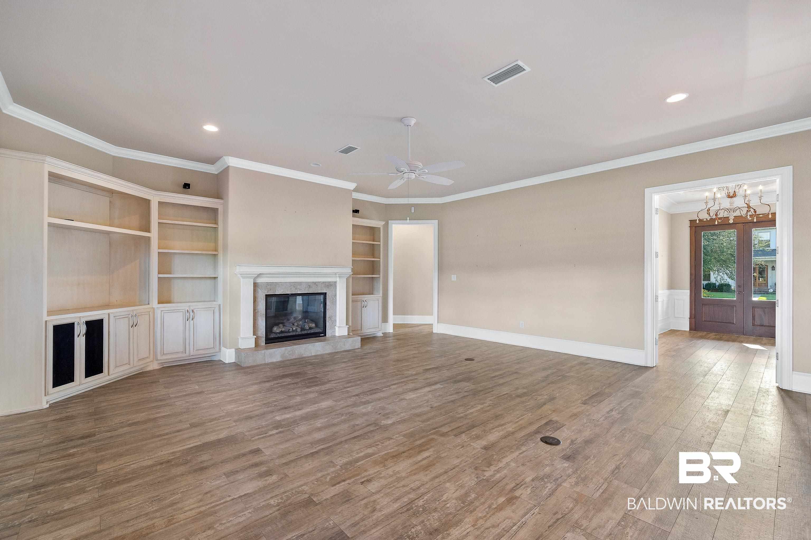 17663 Burwick Loop Fairhope, AL 36532 - Photo 9 of 41 Unfurnished living room featuring ceiling fan with notable chandelier, a high end fireplace, crown molding, built in shelves, and hardwood / wood-style floors