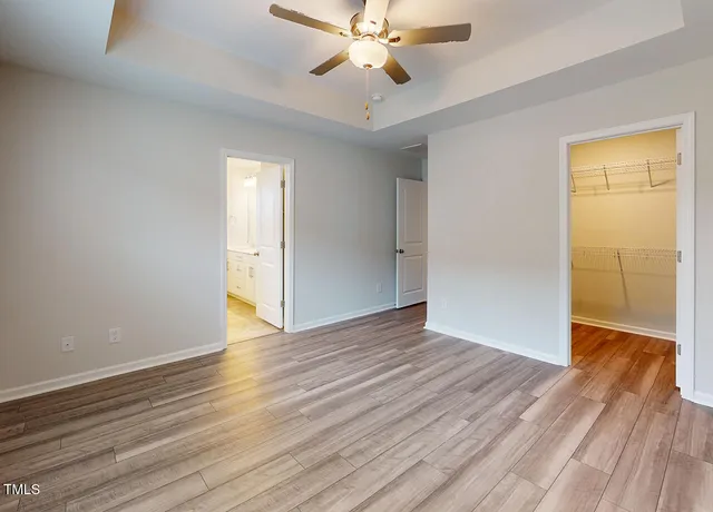 a view of an empty room with wooden floor and a ceiling fan
