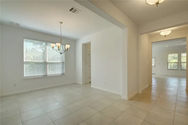 an empty room with chandelier fan and windows