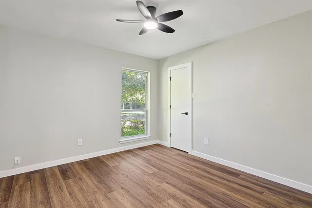an empty room with wooden floor chandelier fan and windows