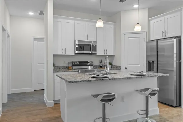 a kitchen with stainless steel appliances granite countertop a sink a stove a refrigerator and island with wooden floor