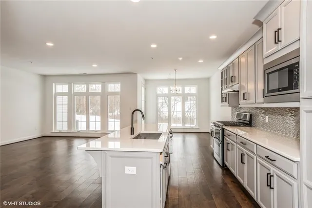 a kitchen with stainless steel appliances a stove top oven a sink a refrigerator white cabinets and wooden floor