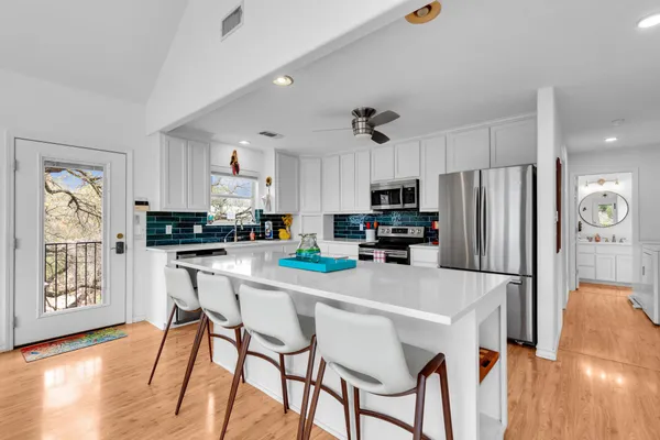 a kitchen with stainless steel appliances granite countertop a refrigerator a sink dishwasher a stove and white cabinets with wooden floor