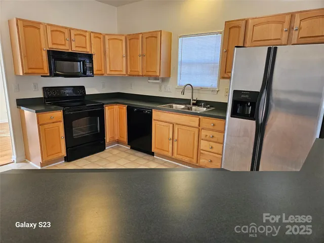 a kitchen with stainless steel appliances a sink a stove a microwave a refrigerator a sink and dishwasher with wooden floor