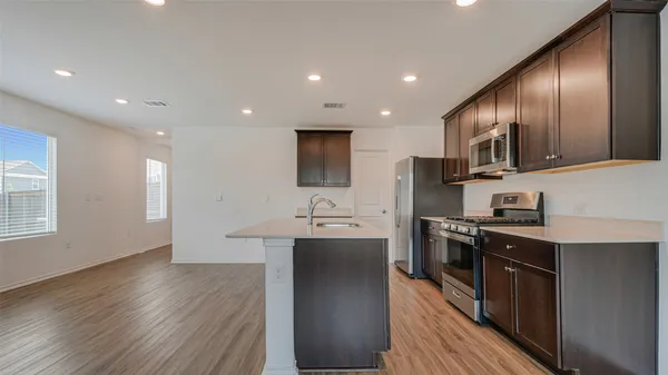 a kitchen with stainless steel appliances granite countertop wooden cabinets a sink dishwasher a stove and a refrigerator with wooden floor