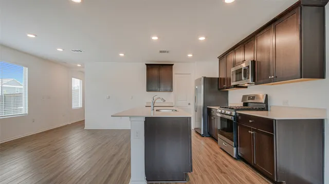 a kitchen with stainless steel appliances granite countertop wooden cabinets a sink dishwasher a stove and a refrigerator with wooden floor