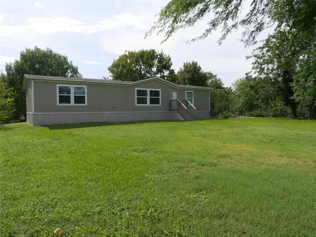 a house that is sitting in the grass with tress in the background