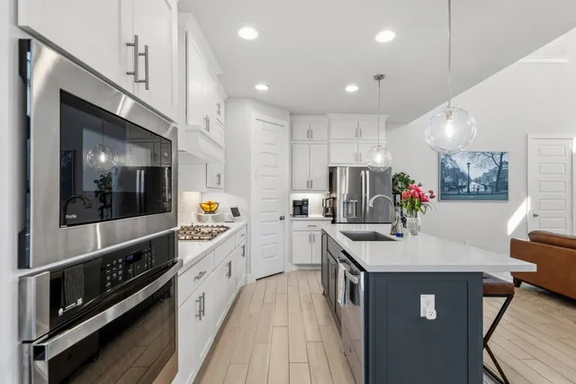 a large kitchen with stainless steel appliances kitchen island granite countertop a large stove a sink dishwasher and white cabinets with wooden floor