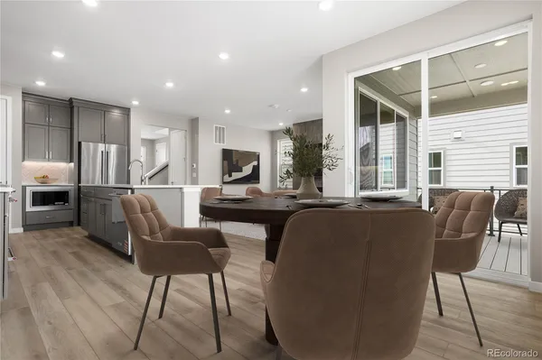 a open kitchen with stainless steel appliances kitchen island granite countertop a refrigerator a stove a dining table and chairs with wooden floor
